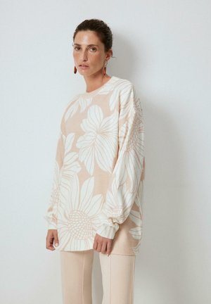 Maglione knit beige chiaro con grandi motivi floreali bianchi. Il design presenta maniche larghe e polsini a costine, con una vestibilità rilassata.