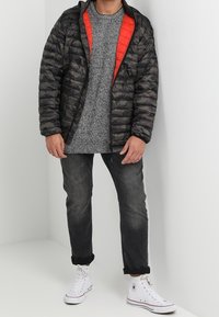 Sort og grå camouflage-dunjakke med røde detaljer, struktureret grå sweater, mørke jeans og hvide high-top sneakers.