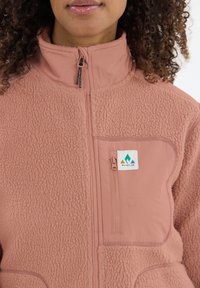 Fleecejack in gedempt roze, met een hoge kraag, ritszak op de borst en een gestructureerde stof met een zachte, donzige afwerking. Logo aanwezig.