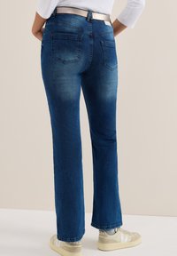Blå denimjeans med rak bendesign, försedda med bakfickor och ett vävt bälte, i kombination med ljusa sneakers.