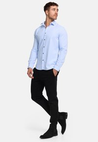 Lichtblauwe overhemden met een gladde textuur, gecombineerd met zwarte slim-fit broek en zwarte suède enkellaarzen. Heeft bruine knopen.