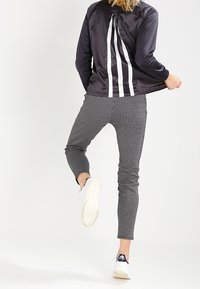 Svart satinjacka med vita ränder, tillsammans med svart och vit rutiga byxor. Skorna är vita sneakers med en mörk logotyp.