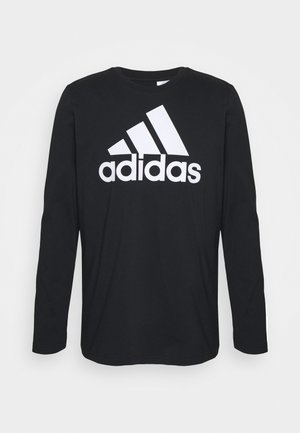 Czarna bawełniana koszulka z długim rękawem i okrągłym dekoltem. Z przodu duże białe logo Adidas. Gładka tekstura.