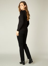 Zwarte langemouwen fitted top gecombineerd met zwarte jeans. De top heeft een gladde textuur, terwijl de jeans een klassieke denimafwerking en subtiele stiksels hebben.