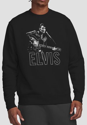 Man wearing black sweatshirt with graphic of Elvis Presley playing guitar and singing into a microphone, with "ELVIS" text below.