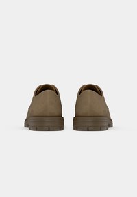 Pair of brown suede shoes with thick rubber soles shown from the back on a plain light gray background.