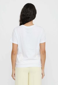 T-shirt bianco in cotone con colletto tondo, maniche corte e vestibilità rilassata. Tessuto liscio, design semplice, mostrato da dietro.