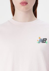 Light pink cotton t-shirt with a round neckline, featuring a textured logo in blue and green with floral and drink motifs on the chest.