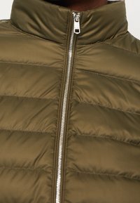 Zielono-oliwkowa, ocieplana kamizelka z wysokim kołnierzem. Posiada pełny zamek błyskawiczny z przodu oraz przeszycia w poziome linie. Gładki, błyszczący materiał.