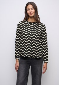 Blusa button-up nera e crema con motivo a zigzag, maniche lunghe e scollatura tonda. Il tessuto è leggero e liscio.