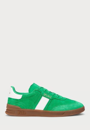 Zielony zamszowy sneaker z białym paskiem i pętelką na pięcie, brązowa podeszwa, logo Polo po bokach i na pięcie, widziany z zewnętrznej strony.