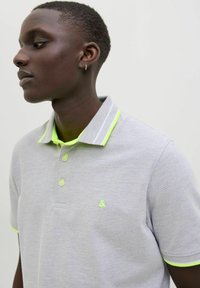 Graues Poloshirt aus strukturiertem Stoff mit einem neongelben Kragen und Akzenten. Drei Knöpfe vorne und ein Logo auf der Brust.