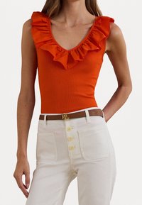 Röd, rynkad linne med V-ringning, kombinerad med krämfärgade, högmidjade byxor med knappslå och ett brunt bälte med en guldfärgad logga.