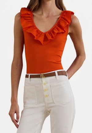 Rode, gerimpelde tanktop met V-hals, gecombineerd met crèmekleurige, high-waisted broek met ritsknopen en een bruine riem met een gouden logo.