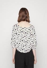 Blusa solta em tecido leve e claro com bolas pretas, apresentando mangas dolman e um amplo decote barco.