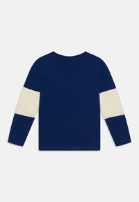 Maglietta a maniche lunghe blu navy con strisce crema sulle maniche, colletto rotondo e morbido materiale in cotone. Design semplice con retro di colore uniforme.