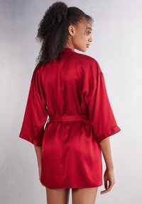 Röd satin kimono-liknande morgonrock med korta ärmar, ett midjeband och en mjuk textur, som visar en flödande design och elegant finish.