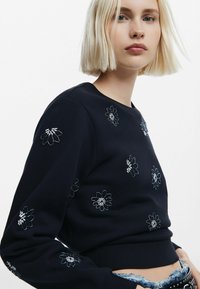 Felpa navy con ricamo floreale in filo d'argento, colletto e polsini a costine, design aderente, texture morbida e lunghezza cropped.