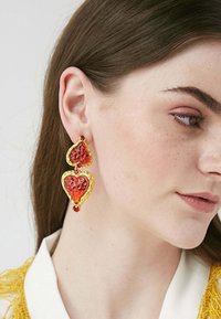 Orecchini in tonalità oro con due cuori sovrapposti in resina rossa texturizzata, arricchiti da piccole gemme rosse per un tocco di dettaglio in più.