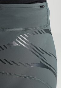 Szare legginsy sportowe o gładkiej strukturze i wysokim staniku. Czarne metaliczne paski tworzą dynamiczny wzór wzdłuż boku.