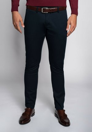 Ciemnoniebieskie spodnie o slim fit z bawełny, z brązowym skórzanym paskiem z stalowym klamrą, w połączeniu z brązowymi butami.