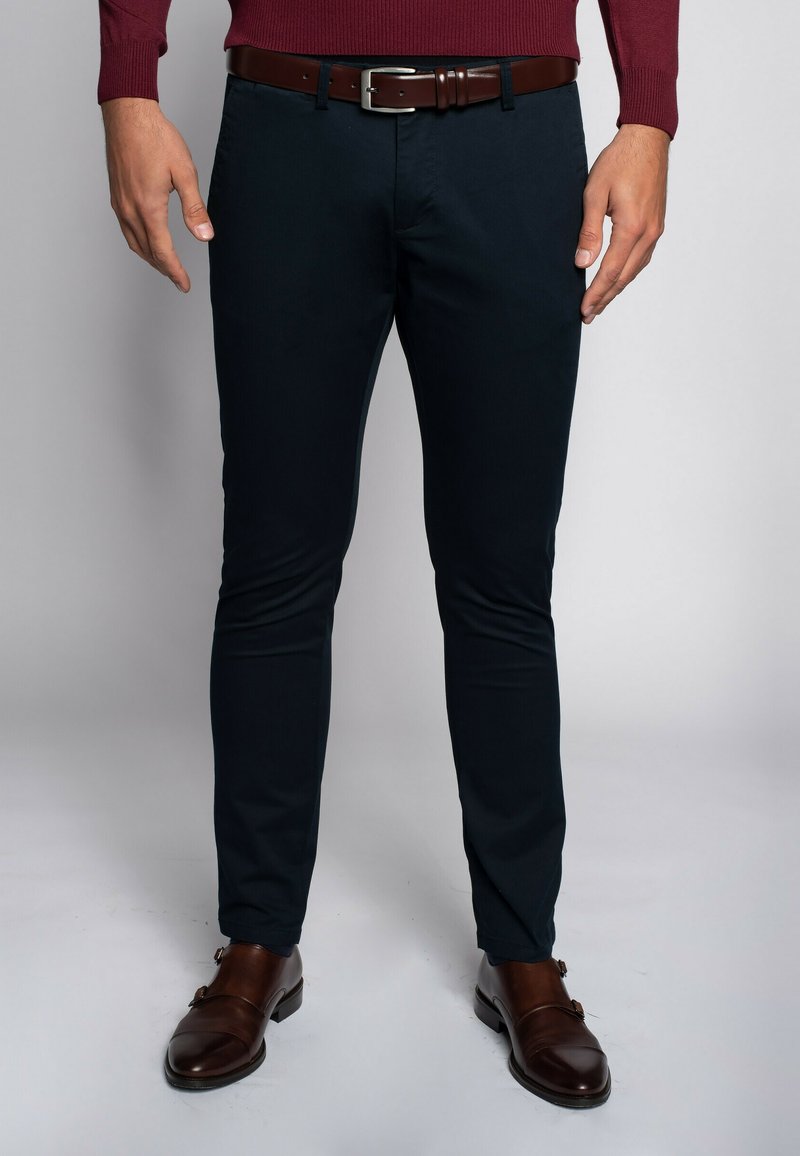 Ciemnoniebieskie spodnie o slim fit z bawełny, z brązowym skórzanym paskiem z stalowym klamrą, w połączeniu z brązowymi butami.