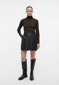 Maglione a collo alto marrone, mini gonna nera in pelle con bottoni e stivali alti neri in pelle. Design minimalista su uno sfondo semplice.
