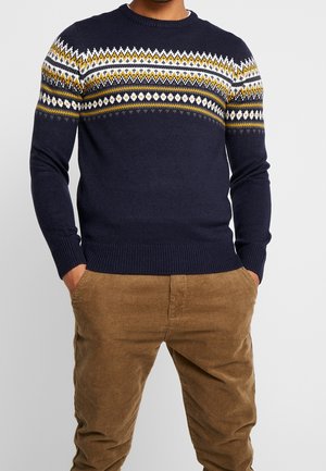 Suéter de punto azul marino con un patrón geométrico en amarillo, blanco y gris a lo largo del pecho, con puños y dobladillo acanalados.
