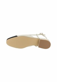 Beige sandal med remmer og flat såle, med en teksturert gummibase, svart tåhette og ankelspenne for sikker lukking.