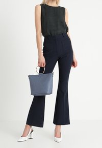 Svart ärmlös topp med vita prickar, hög midja havsblå utsvängda byxor, vita klackar och en grå handväska med ett runt handtag.