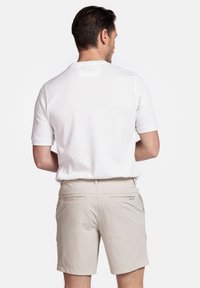 Witte polo met korte mouwen, beige shorts met twee achterzakken, platte tailleband, gladde textuur, minimalistisch ontwerp.