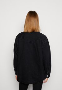 Yli suuri musta farkkupaita pitkillä hihoilla, napillisilla hihansuilla ja kärjellä varustetulla takakappaleella. Pehmeä rakenne, rento muotoilu.