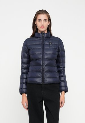 Marineblauwe pufferjack met horizontaal gestikt ontwerp, hoge kraag, frontzipper en een subtiele logodetail op de borst. Lichtgewicht stof.