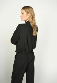 Mustat lyhyet takit, joissa on joustava vyötärö, sileä pinta ja pitkät hihat. Yhdistetty mustiin leveälahkeisiin housuihin, joissa on minimalistinen muotoilu.