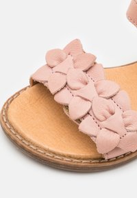 Blush rosa lær sandaler med en dekorativ blomsterstropp med teksturerte kronblad, en glatt tan fotseng, og sydd brun yttersåle.