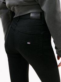 Svarta denimjeans med hög midja, med ett texturerat märke med "TOMMY JEANS" och en liten logodetalj på bakfickan.