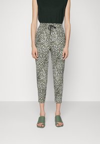 Spodnie z regulowanym paskiem w talii w wzór w panterkę, w kolorach zielonym, czarnym i białym. Dopasowane do zielonych sandałów typu klapki.