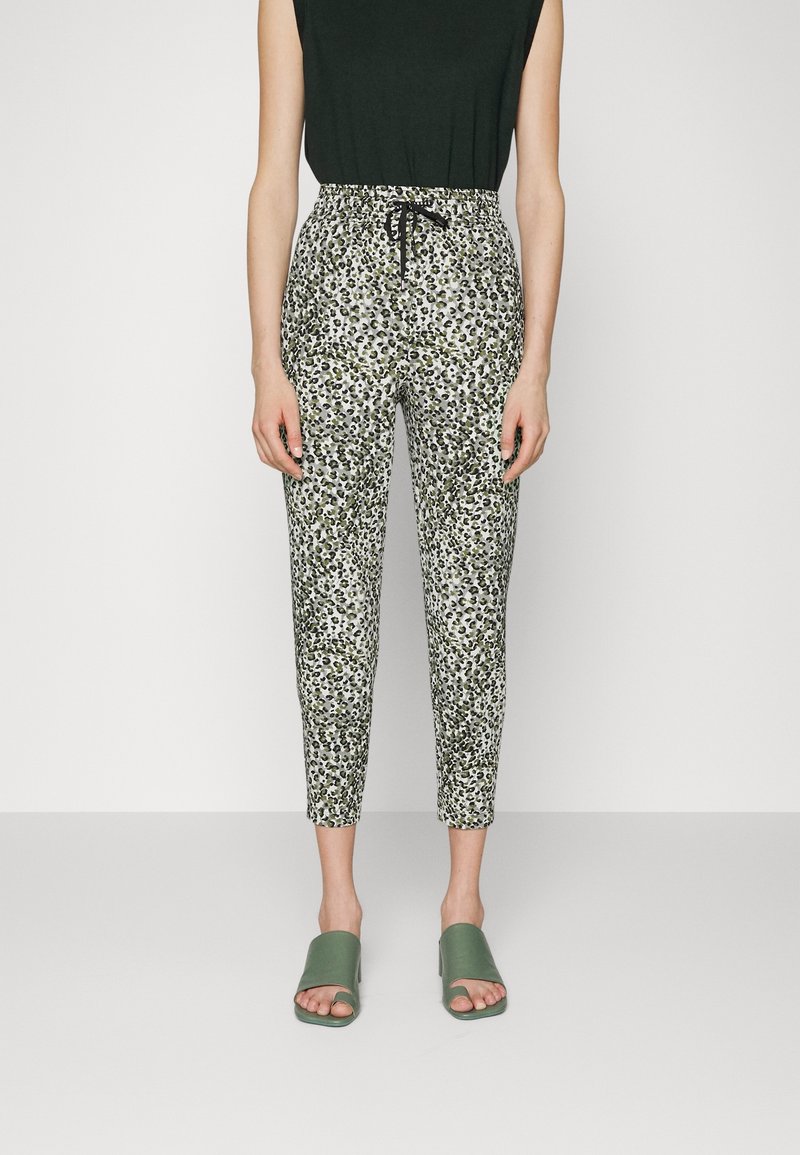 Spodnie z regulowanym paskiem w talii w wzór w panterkę, w kolorach zielonym, czarnym i białym. Dopasowane do zielonych sandałów typu klapki.