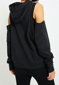 Zwarte oversized hoodie met uitsparingen op de schouders en een capuchon. Zacht stof, losse pasvorm, geribde details bij de manchetten en de onderrand. Aangepaste lengte aan de achterkant.