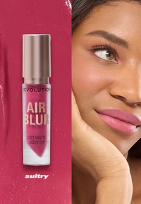 Mjuk matt flytande läppstift i en rosa tube med ett guldlock, märkt "AIR BLUR," bredvid en närbild av en modell med rosa matta läppar.