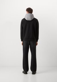 Sudadera negra con capucha gris, con un corte holgado y puños de canalé. Combinada con jeans oscuros de corte amplio y zapatos negros.