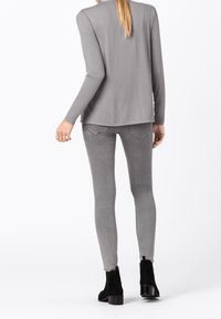 Maglietta grigia a maniche lunghe con orlo arrotondato, abbinata a jeans skinny grigi e stivaletti neri. Tessuto liscio e leggero con un design semplice.