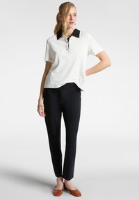 Polo shirt bianco con colletto nero, maniche corte e apertura con bottoni; abbinato a pantaloni neri e ballerine marroni. Texture liscia.