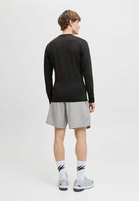 Schwarzes langärmeliges Sportshirt, graue Shorts, graue Sportschuhe und gemusterte weiße Socken; minimalistisches Design mit weicher Textur.