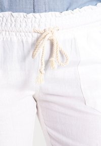 Witte linnen broek met een elastische tailleband, voorzien van een aantrekkoord van beige touw en zijzakken. Gelijke, gladde textuur over de hele broek.