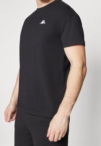 Černé bavlněné tričko s kulatým výstřihem a krátkými rukávy. Obsahuje malé bílé vyšívané logo na hrudi. Přiléhavý design.