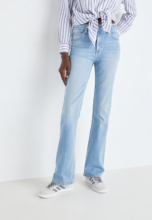 Lys blå flare jeans med fem lomme-desing, rå nederkant og medium vask. Bæres sammen med grå og hvide sneakers og en blåstribet skjorte.