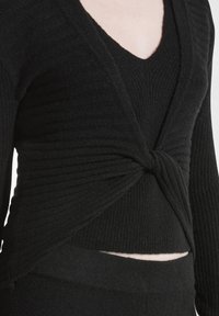 Schwarzer Strickpullover mit gerippter Textur, V-Ausschnitt und gedrehtem Designelement. Verfügt über lange Ärmel und eine verkürzte Passform, die die Taille betont.