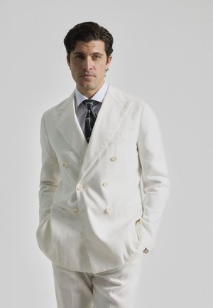 Chaqueta de traje blanca de doble botonadura con solapa muesca, confeccionada en una tela ligera, combinada con una corbata a rayas y una camisa clara.