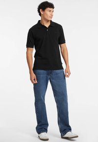 Polo shirt nero con maniche corte e colletto, abbinato a jeans in denim blu e sneakers bianche. Presenta una texture liscia e un design semplice.